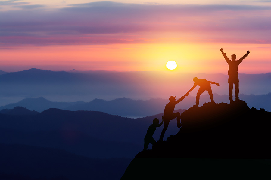 Des individus s’aident à monter une montagne devant un coucher de soleil