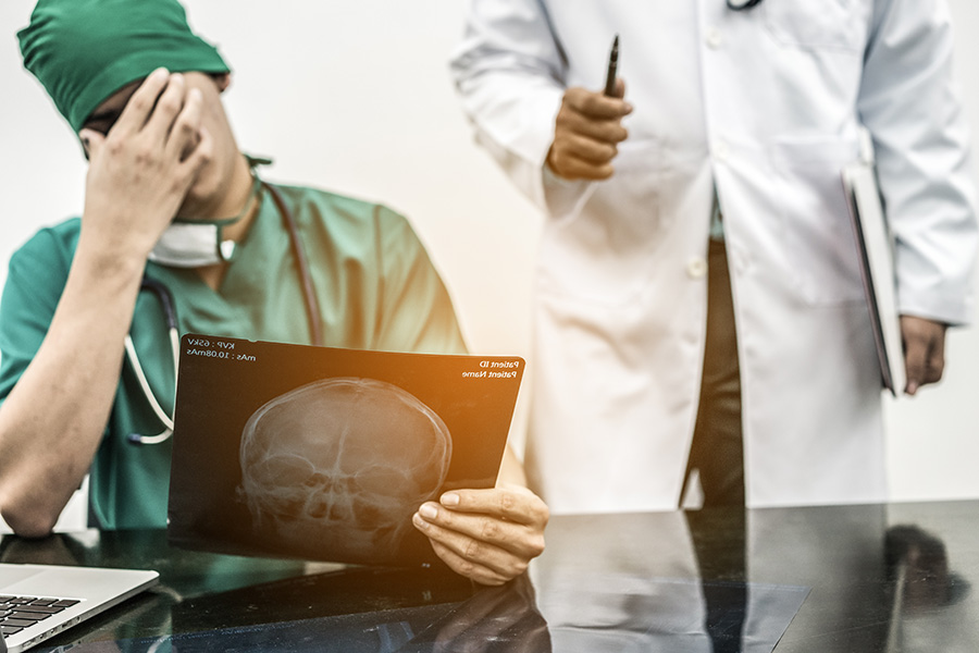 Un professionnel regarde une radiographie en portant sa main à son front, l’air découragé.