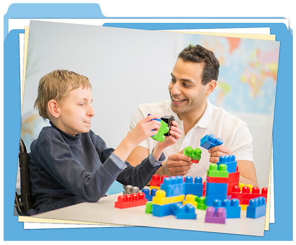 Un professionnel souriant joue aux blocs avec un enfant en fauteuil roulant