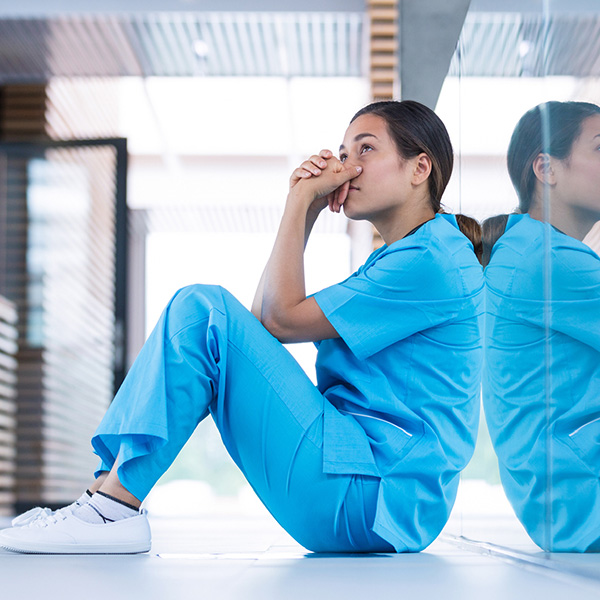 Une professionnelle de la santé est assise par terre avec les coudes appuyés sur ses genoux et regarde au loin.