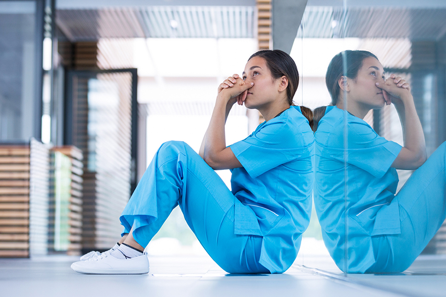 Une professionnelle de la santé est assise par terre avec les coudes appuyés sur ses genoux et regarde au loin