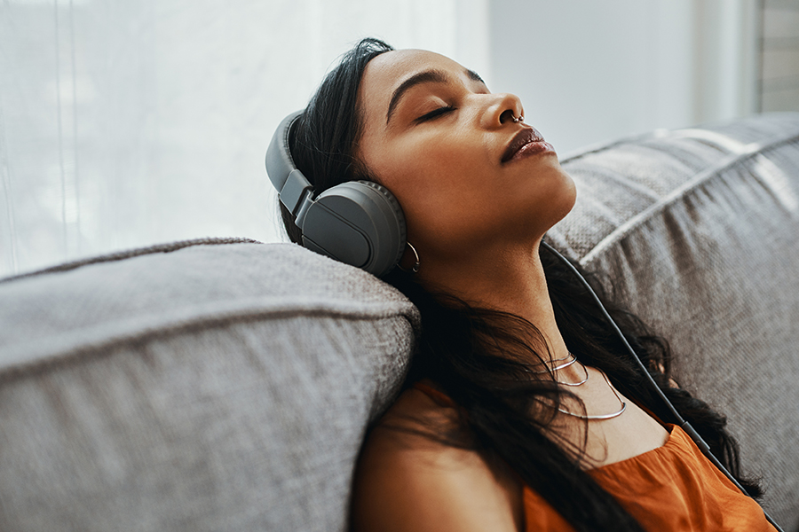 Une femme la tête appuyés vers l’arrière écoute de la musique avec des écouteurs