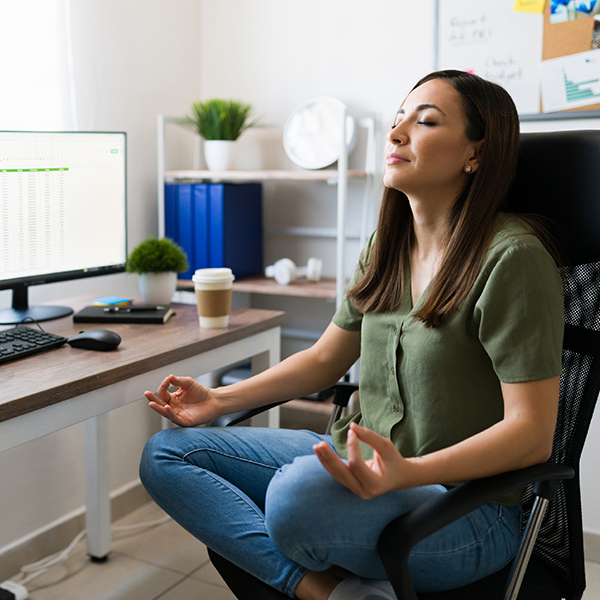 Une jeune femme médite les jambes croisées sur sa chaise de travail avec les yeux fermés