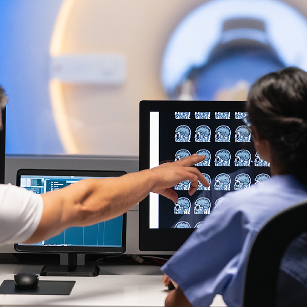 Deux professionnels de la santé regarde l'écran d'une patiente entrant dans une machine IRM..