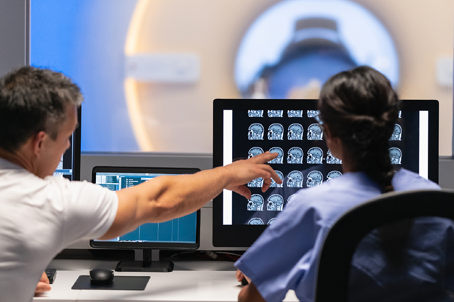 Deux professionnels de la santé regarde l'écran d'une patiente entrant dans une machine IRM.