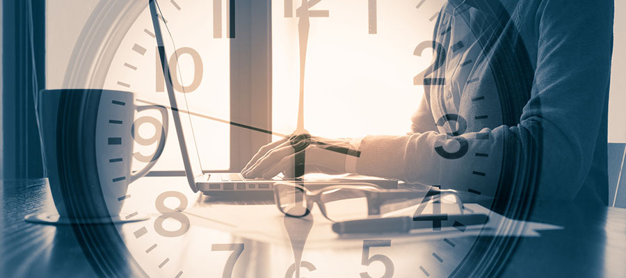 Une horloge est posée sur l’image en arrière-plan d‘une superviseur travaillant à son ordinateur.