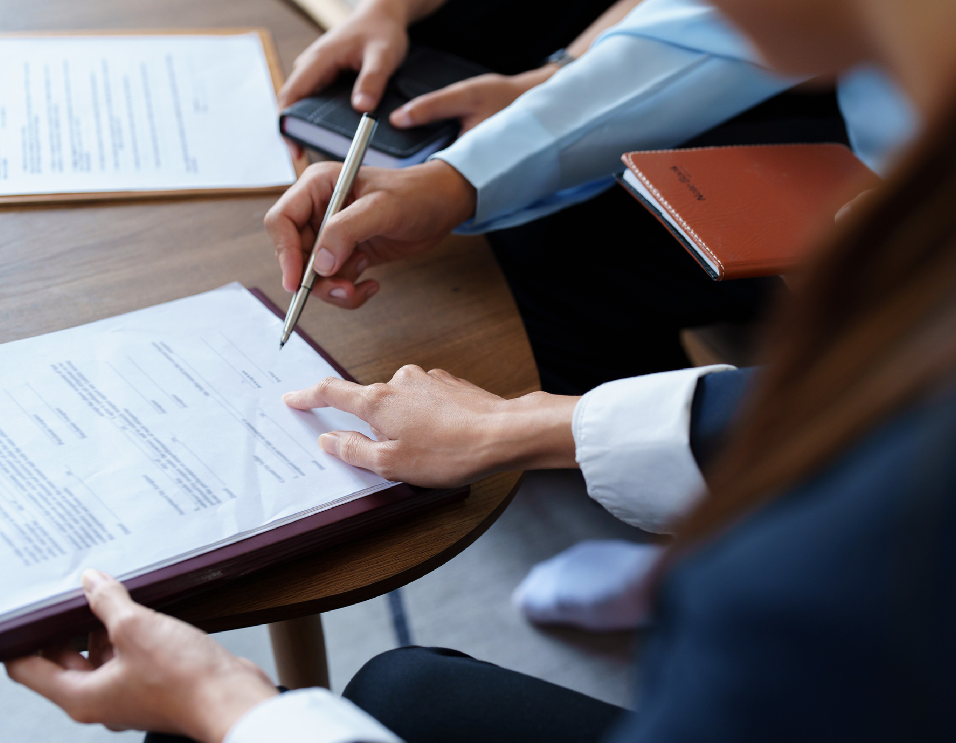 Le superviseur indique l'endroit où le stagiaire doit signer. Le stagiaire tient un stylo et s'apprête à signer. La personne-ressource est avec eux et attend son tour pour signer