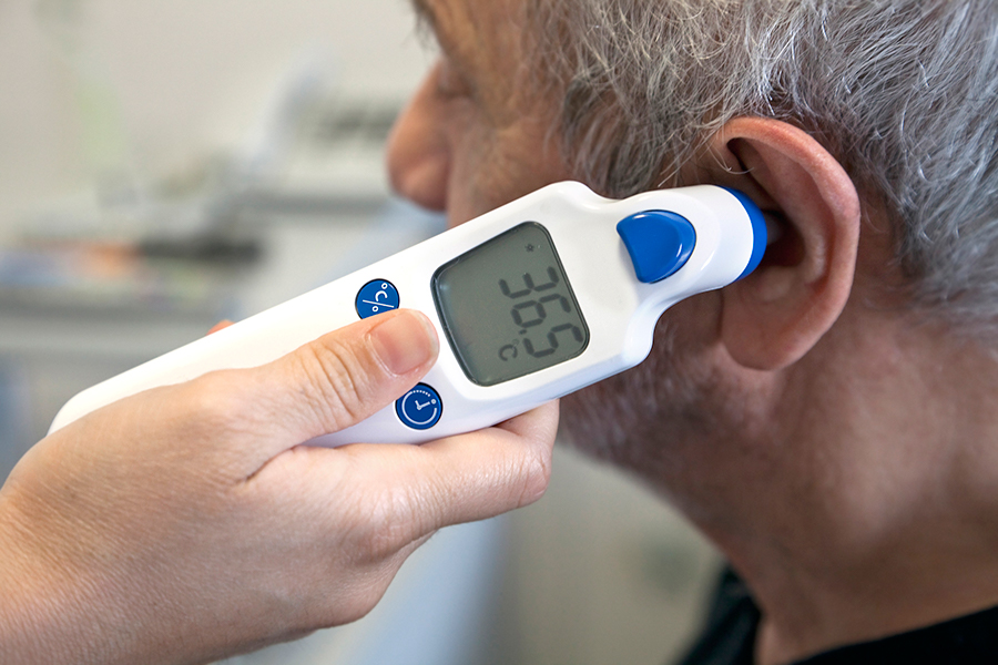 Une infirmière prend la température d’un homme par l’oreille avec un thermomètre numérique 