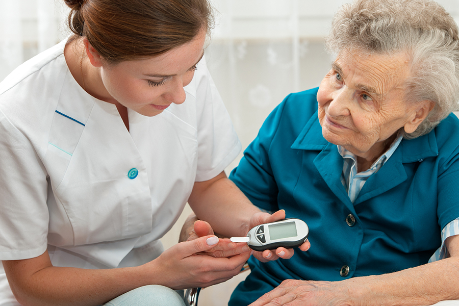 Une infirmière aide sa patiente âgée qui est diabétique utilise son glycomètre