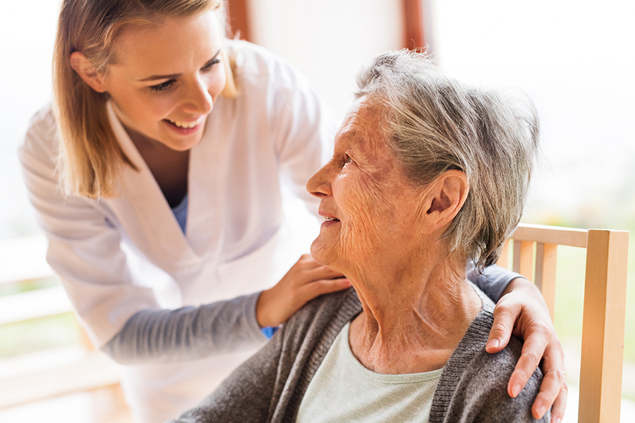 Une clinicienne souriante avec ses mains sur les épaules de sa patiente de 85 ans avec des troubles perceptuels qui sourit aussi