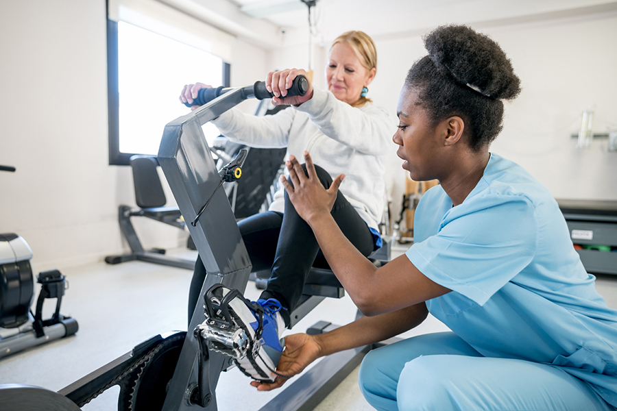 Une physiothérapeute aide sa patiente à mettre son pied sur le pédale d’un vélo stationnaire