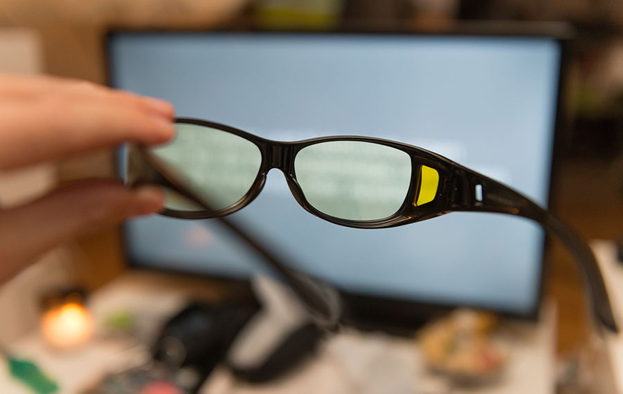 A professional holds glasses in one hand and looks at his computer through the lens.