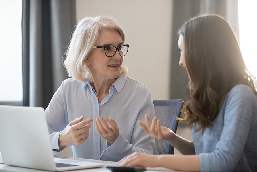 A supervisor is having a discussion with her trainee in front of her computer.