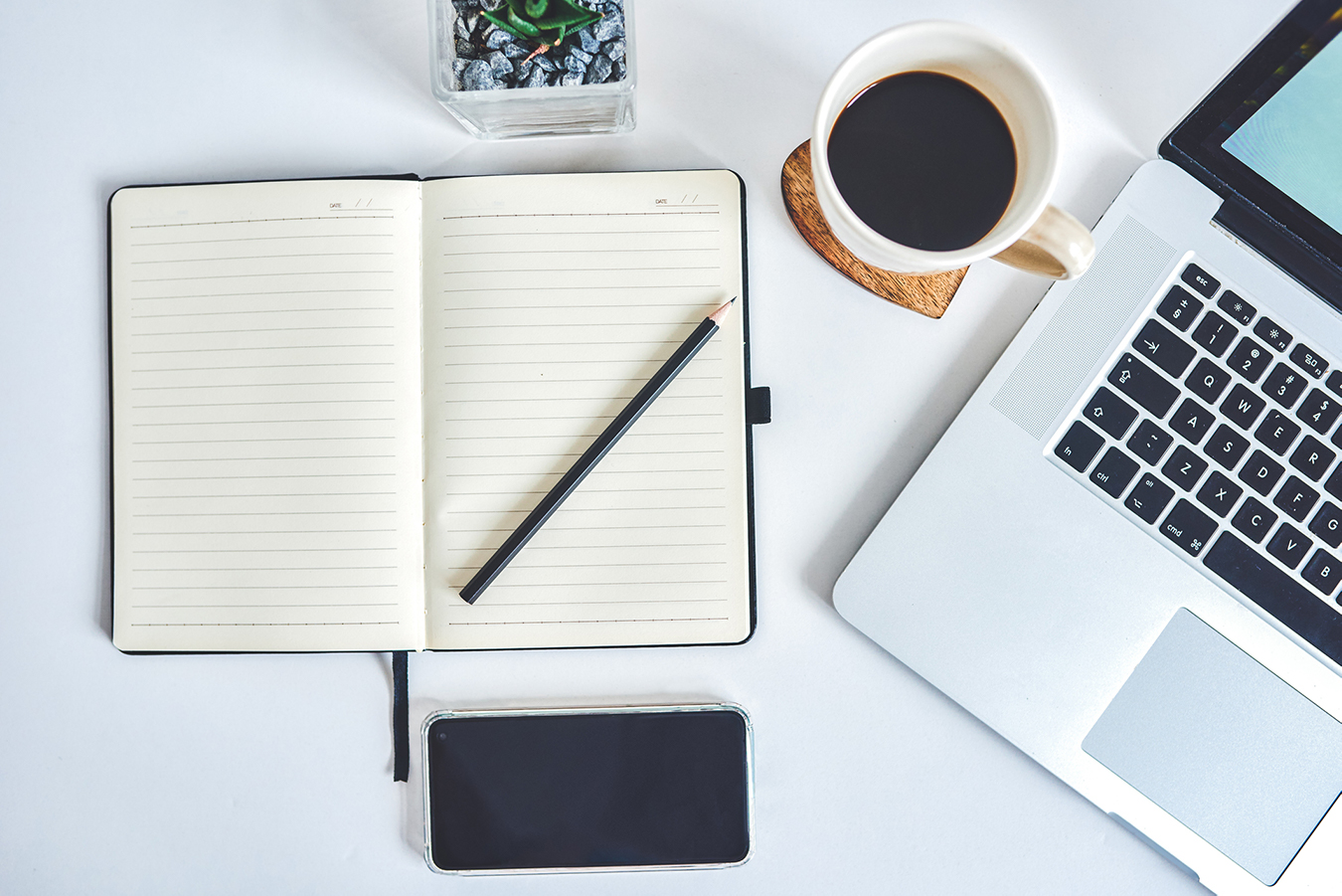 A notebook, a pencil and a computer displayed on a worktable.