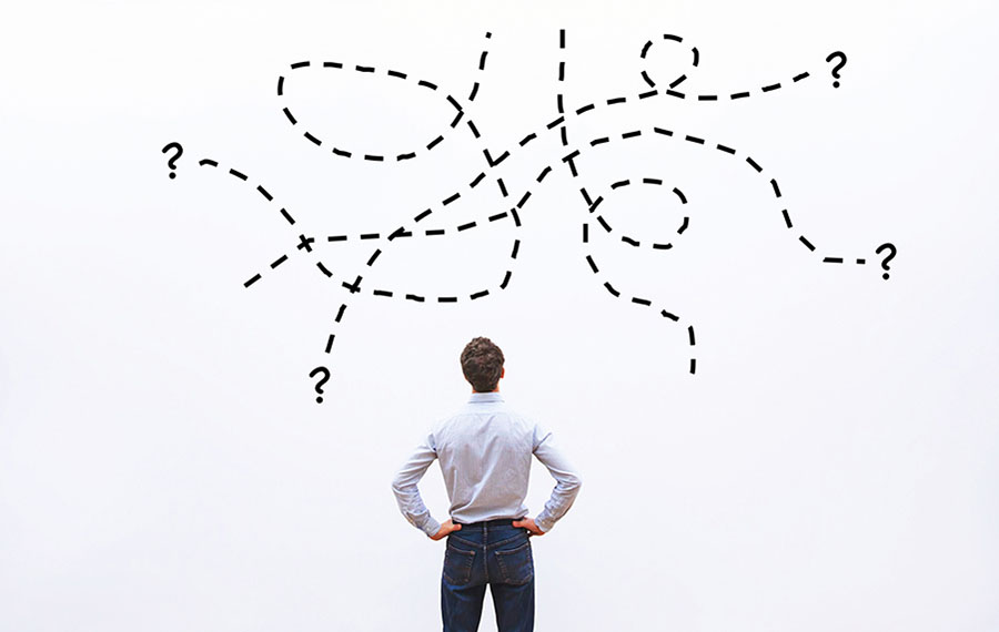 A man is looking at a board in front of him, where different paths end with a question mark.